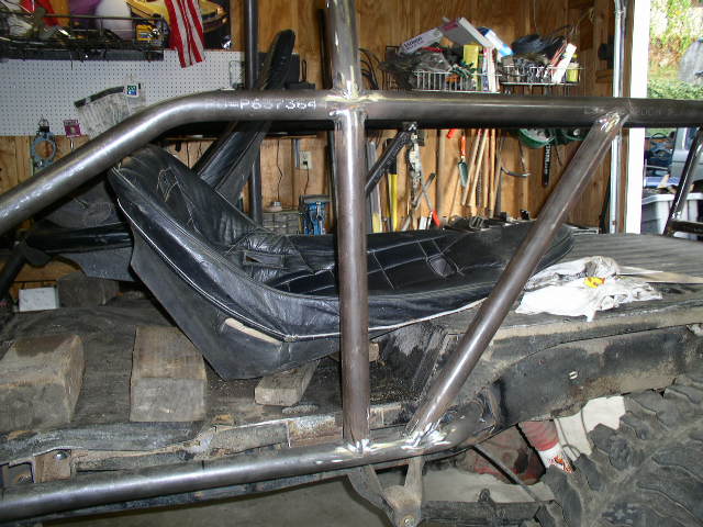 Welded tubular roll cage and black bucket seats on a 4x4 chassis in a garage