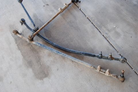 1982 Ford Bronco - Three steering linkage assemblies are laid out on a concrete surface, likely for comparison or sale.