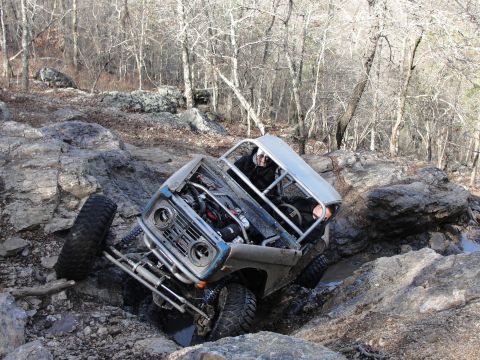 1967 Ford Mustang - An off-road vehicle with a roll cage navigates a challenging rocky obstacle course, its engine visible.