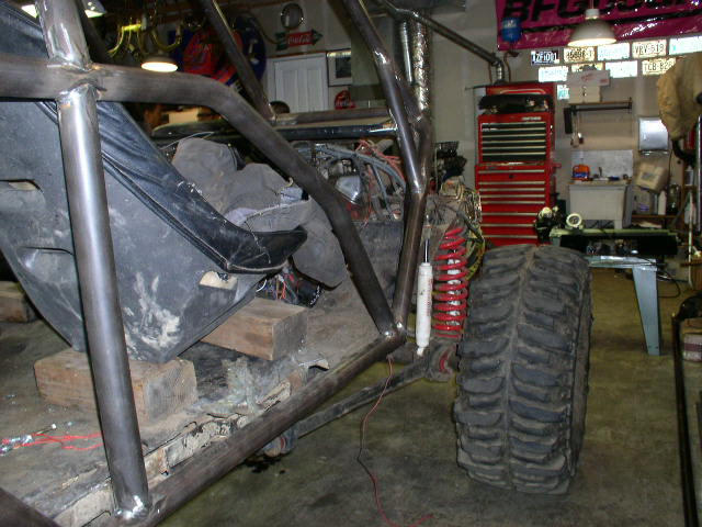 Off-road buggy interior with roll cage, racing seat, and large tire. Garage workshop in background