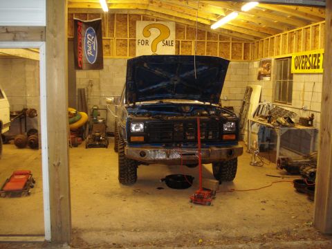 1985 Ford F-150 - A blue pickup truck is parked in a garage with its hood up, undergoing maintenance.