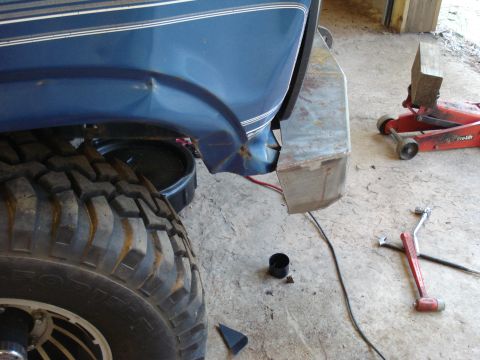 1985 Ford F-150 - The rear quarter panel of a blue truck shows damage, with a large off-road tire and a custom bumper visible.