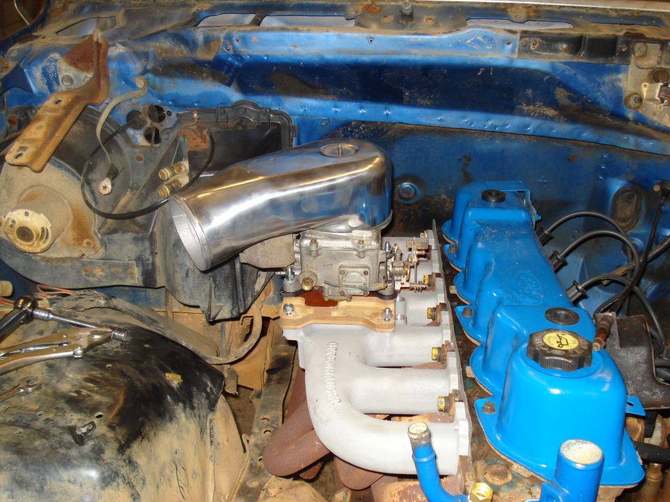 Ford V8 engine block with blue valve covers, carburetor, and chrome air intake. Supermotors.net logo visible