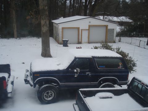 1994 Ford F-350 - A dark blue Ford Bronco sits covered in snow next to a pickup truck in a snowy yard with a garage in the background.