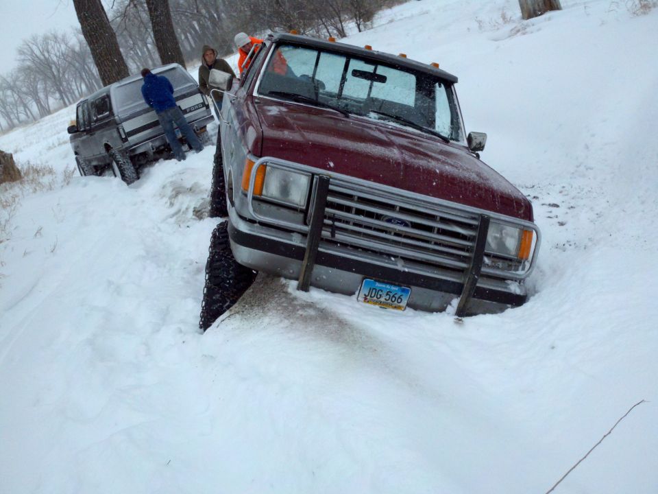 Maroon Ford truck stuck in snow with another truck behind it. License plate JUG 566