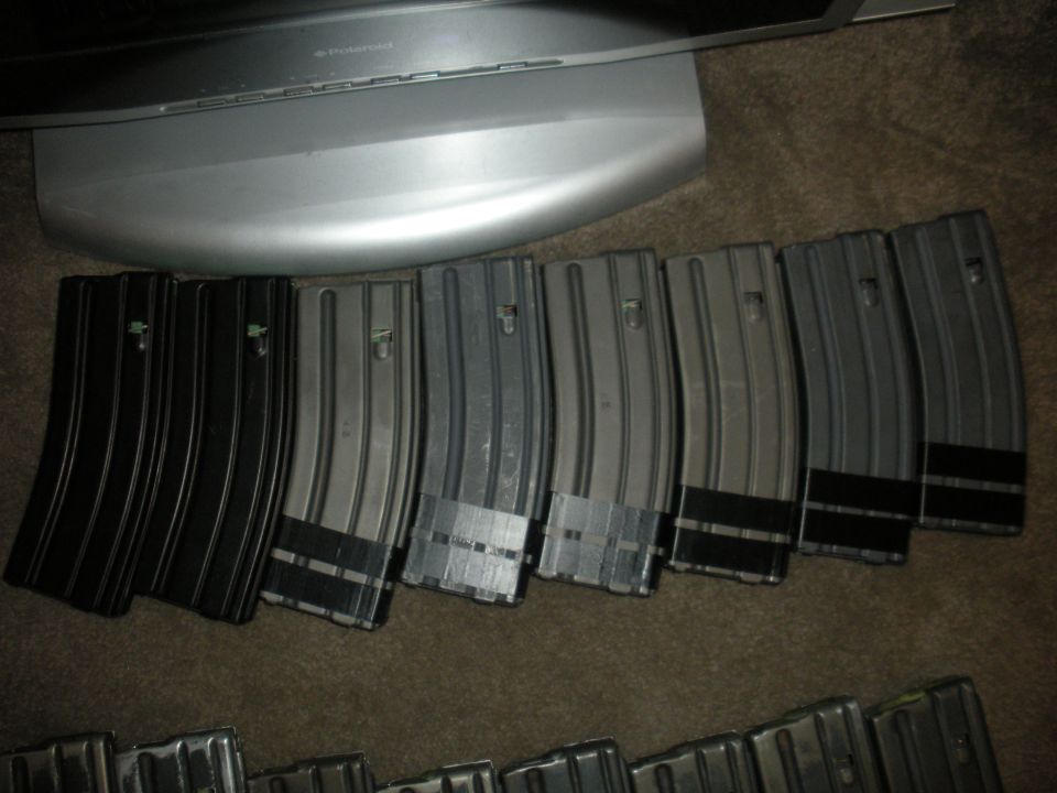 Several black and gray firearm magazines are laid out on a carpeted surface, with a silver monitor stand in the background