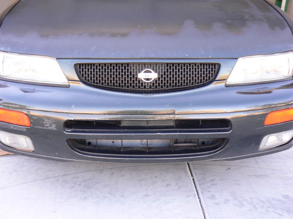Front of a dark-colored Nissan sedan showing the grille with a Nissan badge, headlights, and bumper