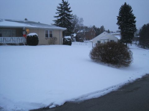 2004 Aston Martin Virage - A residential street is blanketed in snow, with houses and trees visible in the background.