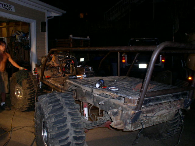 Custom buggy build with large tires and roll cage, a pickup truck in background
