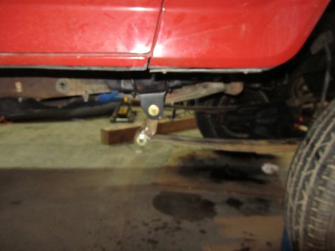 1984 Ford Bronco - The underside of a red vehicle shows rust and a modified suspension component.