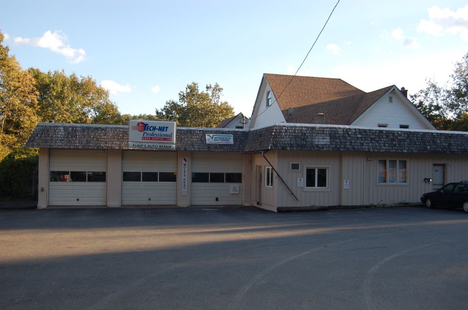 Flint's Auto Repair shop with three garage bays and TECH-NET sign; dark car partially visible at right