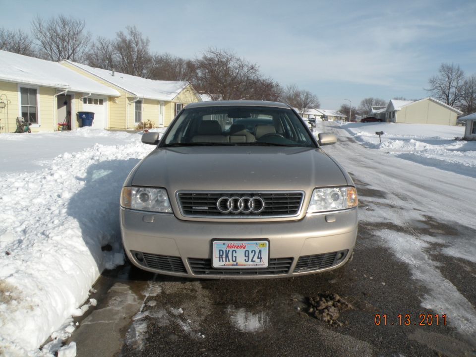 Front view of a gold Audi A6 sedan parked on a snowy residential street
