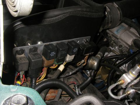 1990 Ford Bronco - A fabricated flat metal relay bracket bolted along the inner fender of an engine bay, carrying six relays including a Bosch 30A unit and Fo…