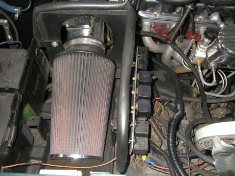 1990 Ford Bronco - Engine-bay shot of a large tapered K&N-style cone air filter on a polished intake tube inside a black airbox shroud, alongside a vertical m…