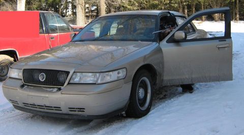 2000 Mercury Grand Marquis - A gold Mercury Grand Marquis is parked in the snow with its driver's door open, beside a red truck.