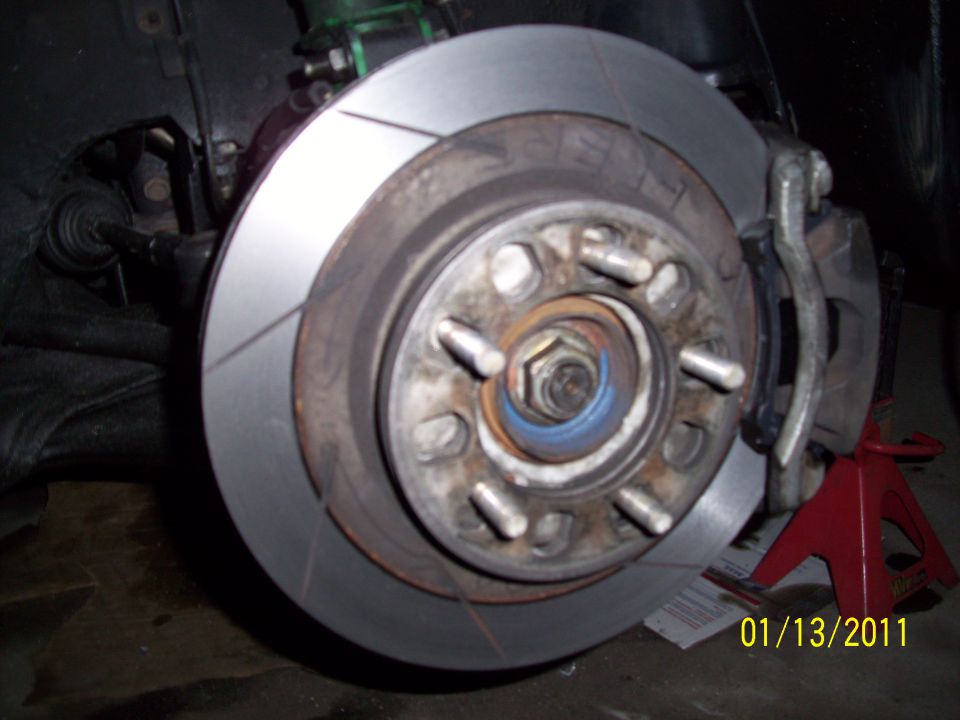 Car brake rotor with caliper and wheel hub, supported by a red jack stand