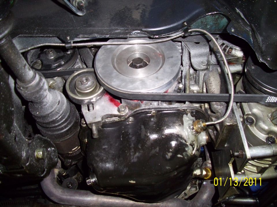 Close-up of a car's engine oil pan with drive belts and pulleys visible. Date stamp reads 01/13/2011