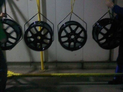 2000 Mercury Grand Marquis - Four black alloy wheels are suspended and appear to be undergoing a coating process.