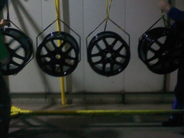 Four black alloy wheels hanging, possibly being painted