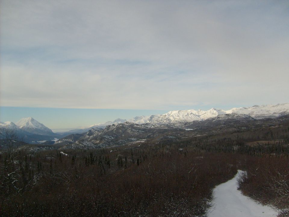 Snowy mountains and forest under a cloudy sky. Watermark reads SUPERMOTORS.NET