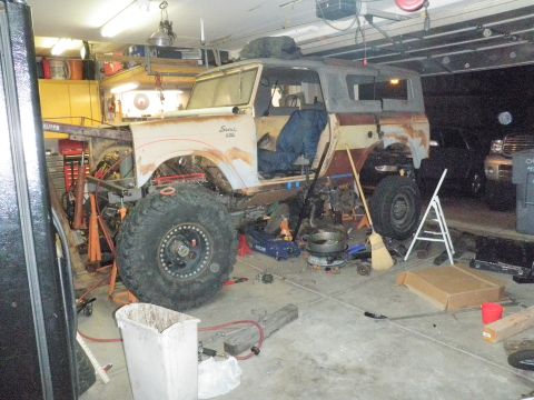 1961 International Scout 800 - A partially disassembled International Scout sits in a cluttered garage, surrounded by tools and spare parts.