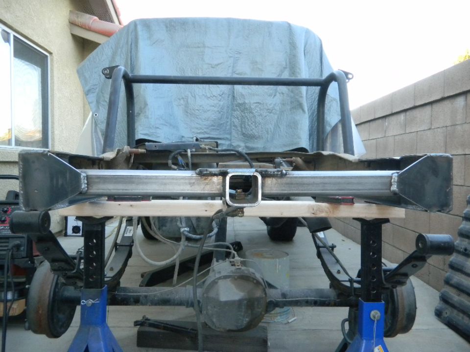 Custom rear bumper and hitch assembly on jack stands, with a tarp covering the vehicle bed