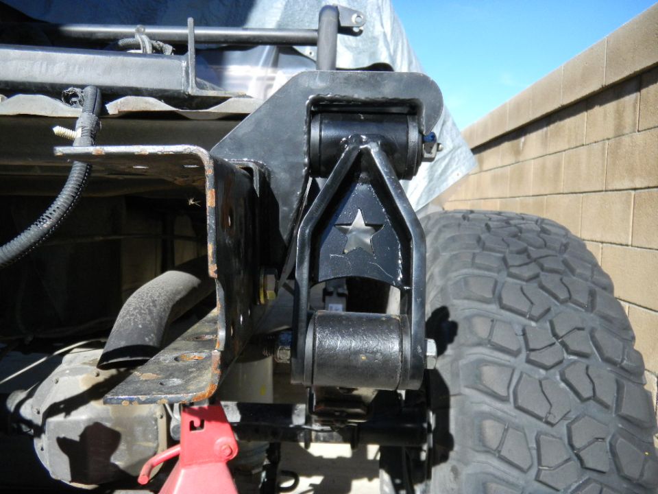 Close-up of a custom suspension component with a star cutout, attached to a truck's rear axle. A red jack stand is visible below