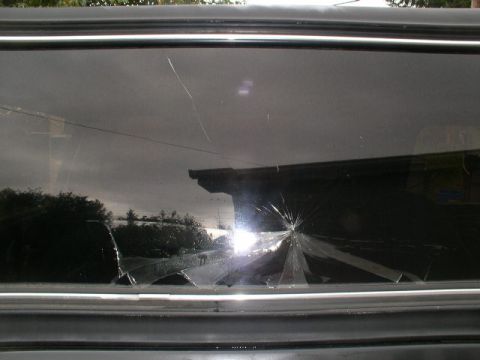 1978 Ford Bronco - Close-up of a broken side or rear window on a dark vehicle, showing a bright starburst impact point with cracks radiating outward across th…