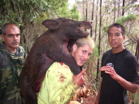 1991 Ford Bronco - A hunter with bleached-blond hair shoulders a large wild boar on a forest trail while two other men stand alongside, one in camouflage rain…
