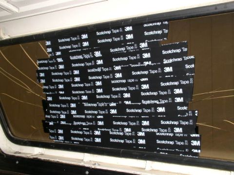 1978 Ford Bronco - A cracked rear side or tailgate window on a vehicle patched with overlapping strips of black 3M Scotchrap tape, with the crack lines still…