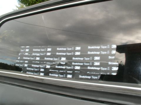 1978 Ford Bronco - Close-up of a dark tinted side window on a black vehicle with overlapping strips of 3M Scotchrap tape applied across the glass as a tempora…
