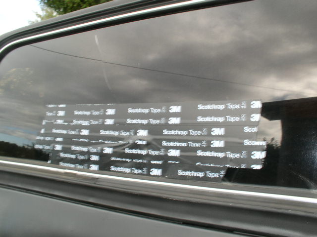 3M Scotchrap tape strips patching a tinted side window on a black vehicle