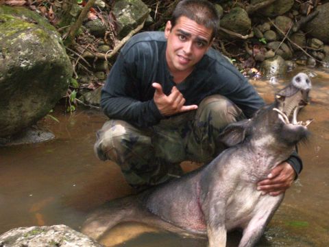 1991 Ford Bronco - A man poses with a wild boar in a natural outdoor setting, with water and rocks visible.