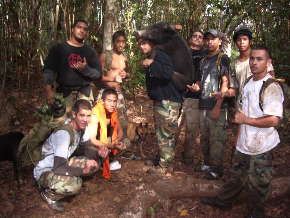 Group of hunters with dogs on a forest trail, one carrying a boar on his shoulders