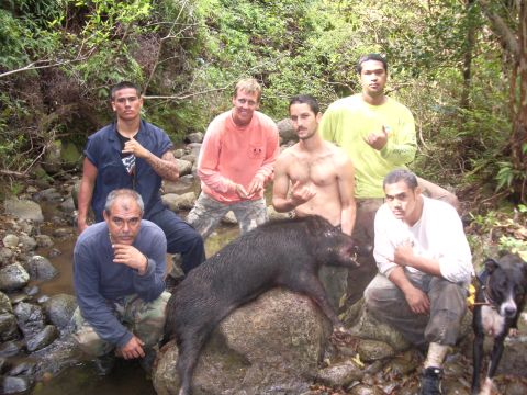 1991 Ford Bronco - Six men and a dog pose with a wild boar carcass in a wooded area next to a stream.