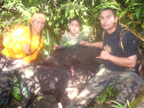 1991 Ford Bronco - Three people pose with a large wild boar they have hunted in a lush, green forest.