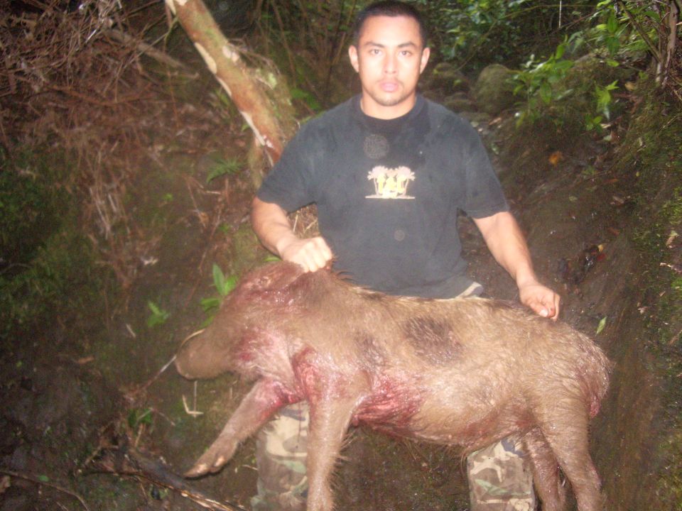 Man with a dead wild boar in a wooded area. Watermark reads SUPERMOTORS.NET