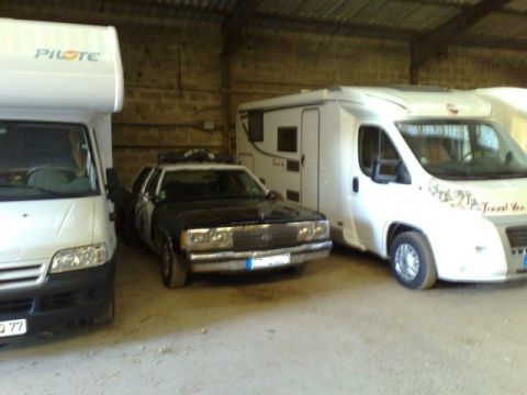 1991 Ford Crown Victoria - A police car is parked between two campers inside a barn.