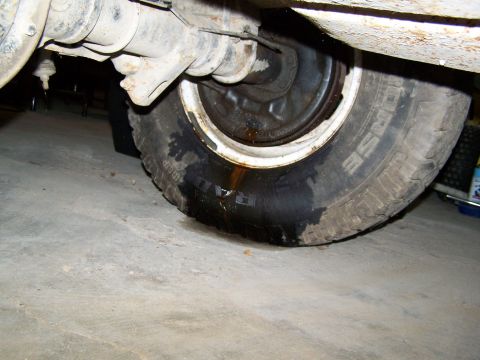 1989 Ford Bronco - A close-up view of a vehicle's undercarriage reveals a tire with a fluid leak onto the garage floor.