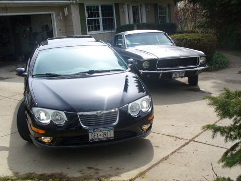 2002 Chrysler 300M - A black 2002 Chrysler 300M is parked in a driveway next to a classic car.