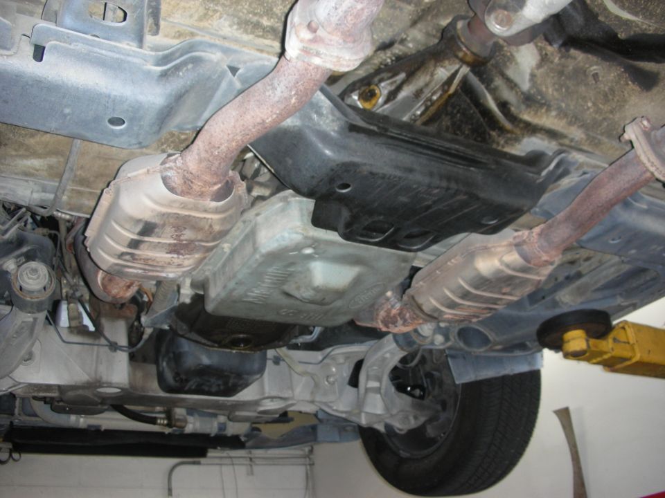 Underside of a vehicle showing exhaust pipes, catalytic converters, and transmission pan