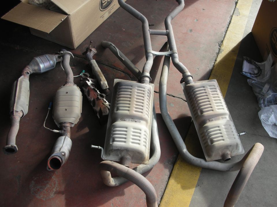 Exhaust system parts including catalytic converters and mufflers laid out on a concrete floor