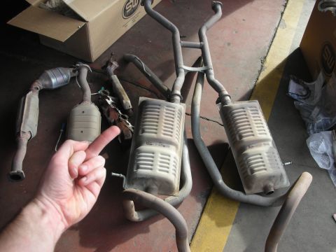 2004 Ford Crown Victoria - Exhaust system parts, including catalytic converters and mufflers, laid out on the floor with a box bearing an "SW" logo in the background.