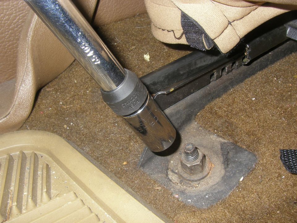 Socket wrench on a seat mounting bolt inside a vehicle. Seat fabric is visible