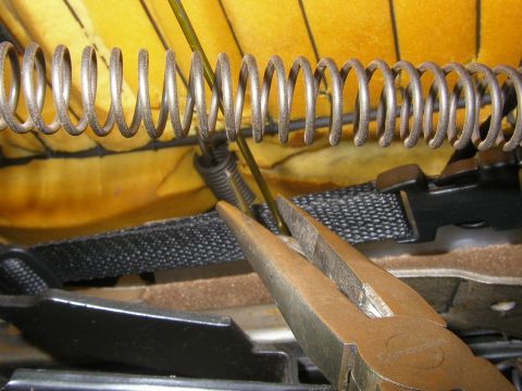 1990 Ford Bronco - Close-up of a seat spring being repaired with pliers, showing internal vehicle seat components.
