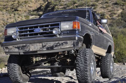 1991 Ford Bronco - This lifted Ford Bronco is navigating a rocky, off-road trail in a desert environment.