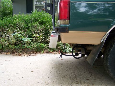 1989 Ford Bronco - Low-angle view of the rear corner of a green-over-tan two-tone Ford SUV, showing the tail light, a swing-away tire carrier bracket, dual ex…