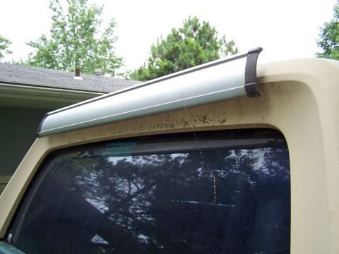 1989 Ford Bronco - Close-up of the rear corner of a tan fiberglass hardtop with an aluminum rear-window air deflector with black end caps mounted above the ti…