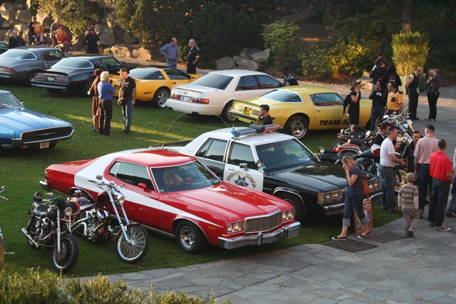 Several cars and motorcycles parked on grass, with people milling around