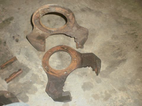 1995 Ford Bronco - These are two rusty metal automotive parts, likely from a vehicle's suspension system, shown on a concrete surface.